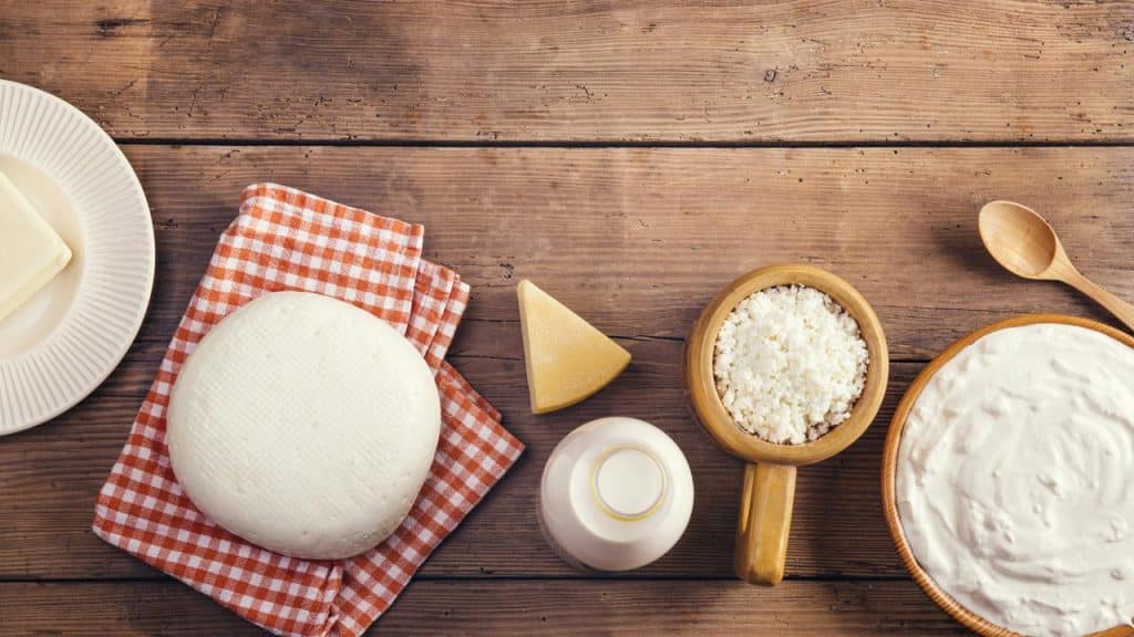 A spread of butter, cheeses, milk, and yogurt on a wooden table.