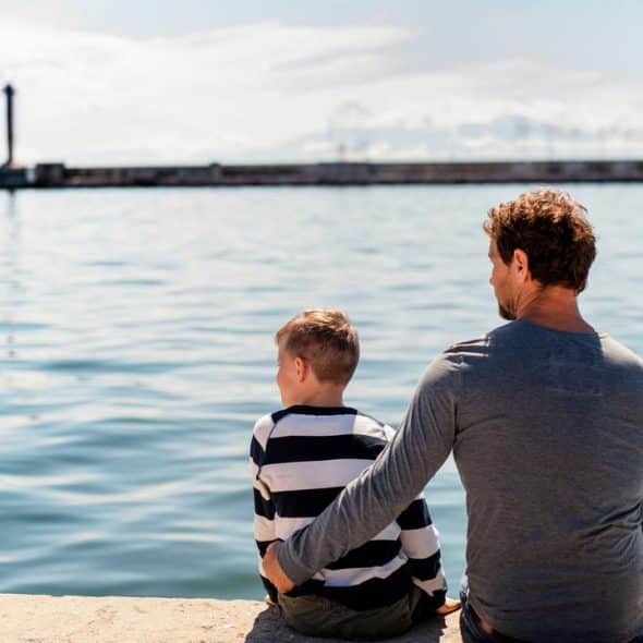 A man and a young boy sitting on a pier, gazing over calm water.