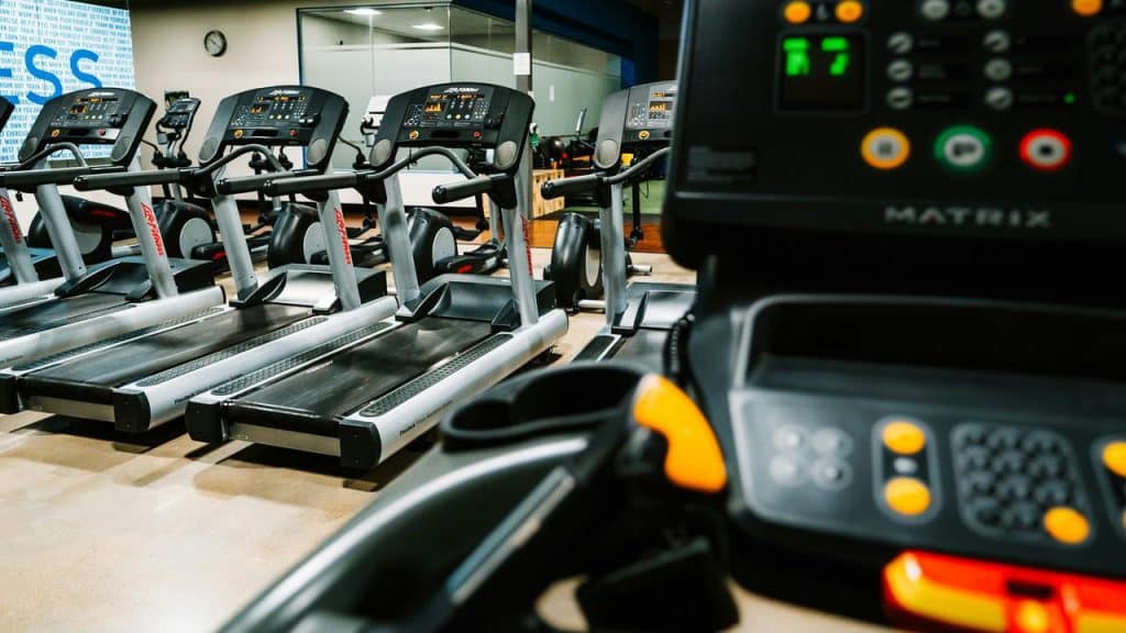 A row of treadmills in a gym, with a control console visible in the foreground.