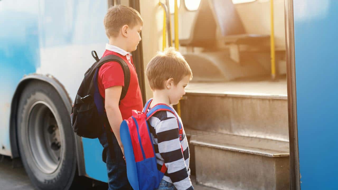 A pair of boys with backpacks boarding a bus.