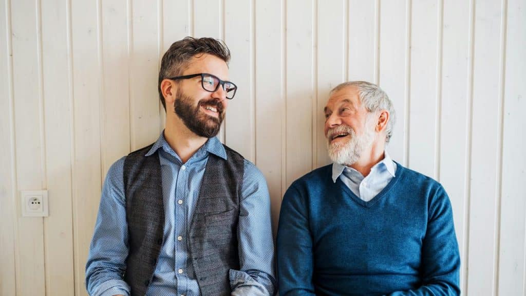 A younger man and an older man smiling at each other.