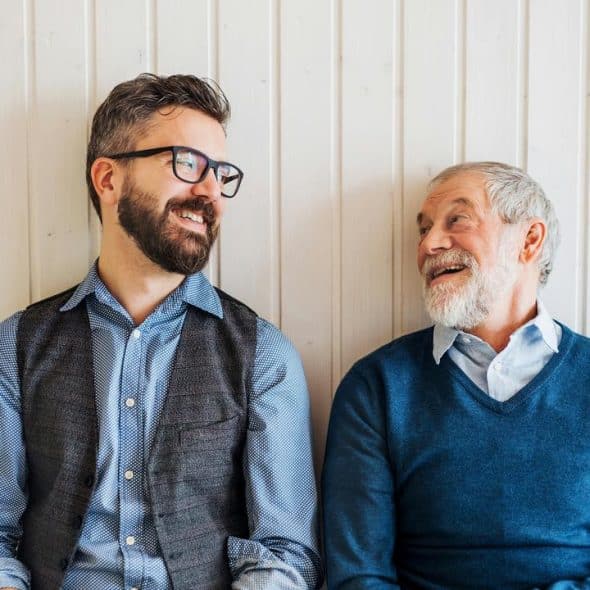 A younger man and an older man smiling at each other.