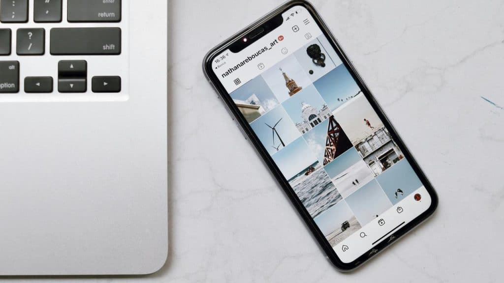 An iPhone displaying an Instagram photo grid beside a laptop keyboard.