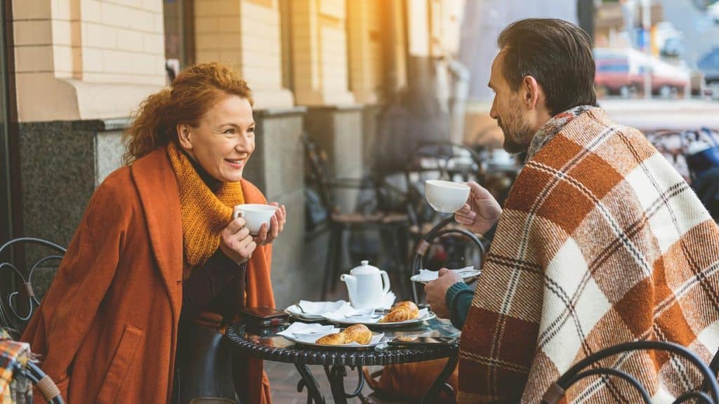 A couple wrapped in blankets enjoying coffee outdoors.