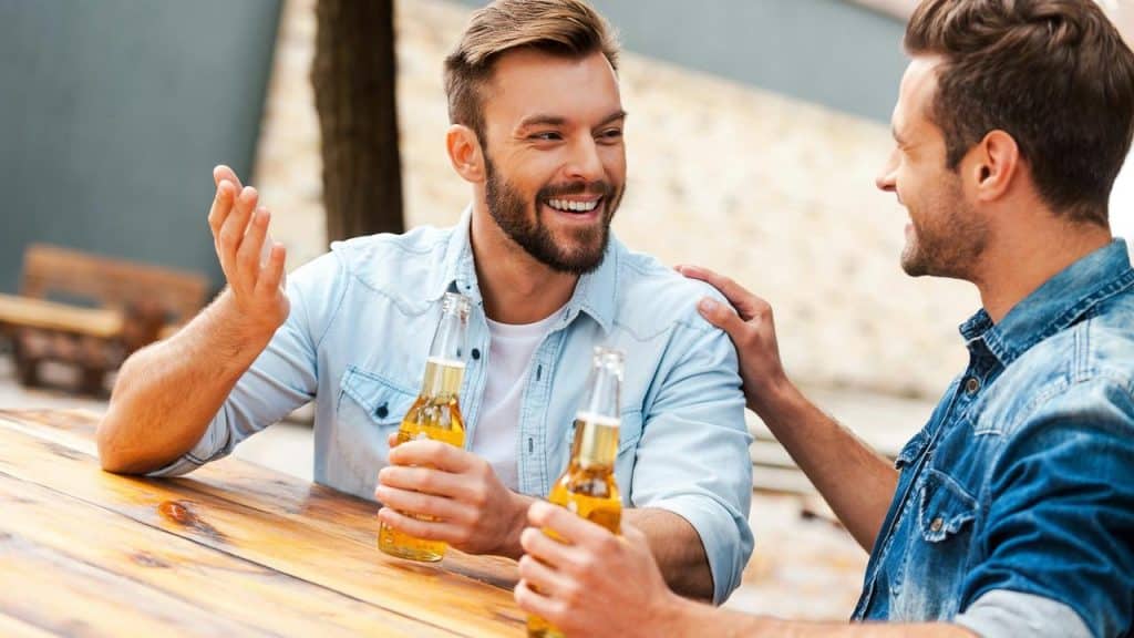 A pair of friends chatting and laughing over beers at an outdoor table.