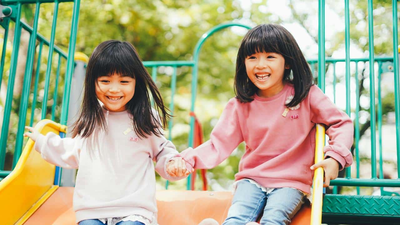 A pair of girls holding hands on a playground slide.