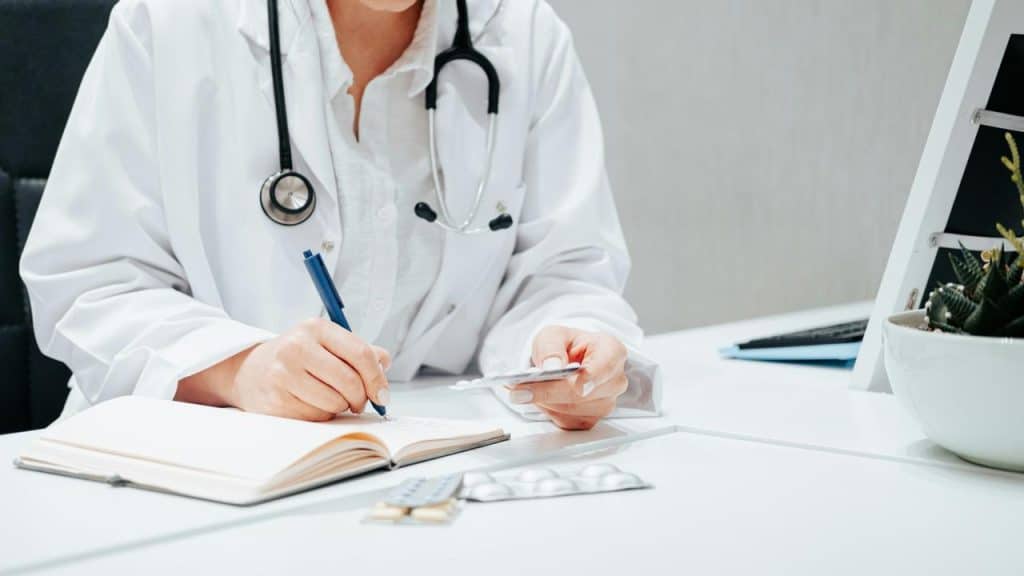 A doctor writing notes while holding a blister pack of pills.