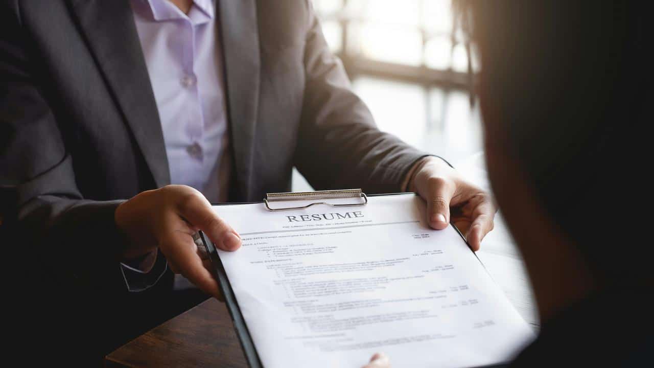 A person handing a clipboard with a resume.