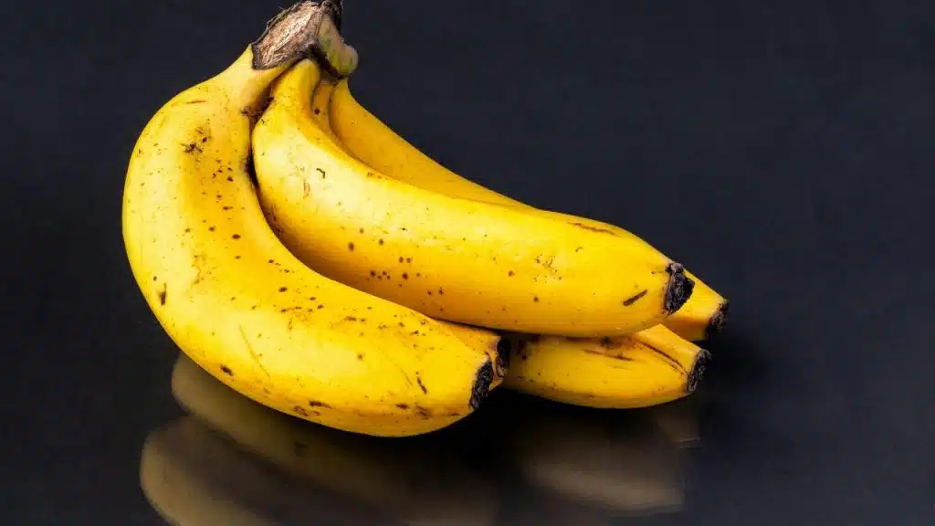 A bunch of ripe yellow bananas resting on a dark reflective surface.