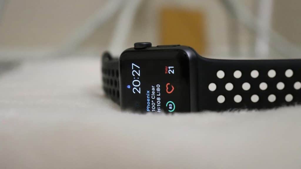 A black smartwatch with a perforated sports band resting on a soft surface.
