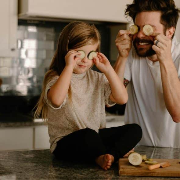 A father and daughter with cucumber slices over their eyes.