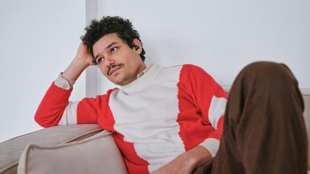 A man in a red and white sweater relaxes on a couch, looking to the side.