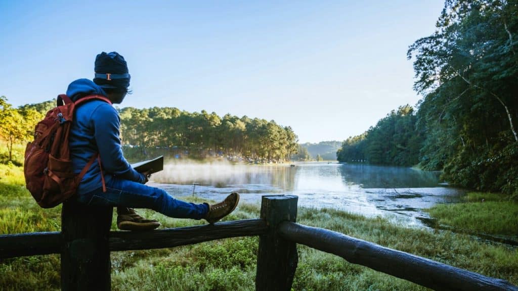A person sits on a wooden fence, looking out at a misty lake and forest.