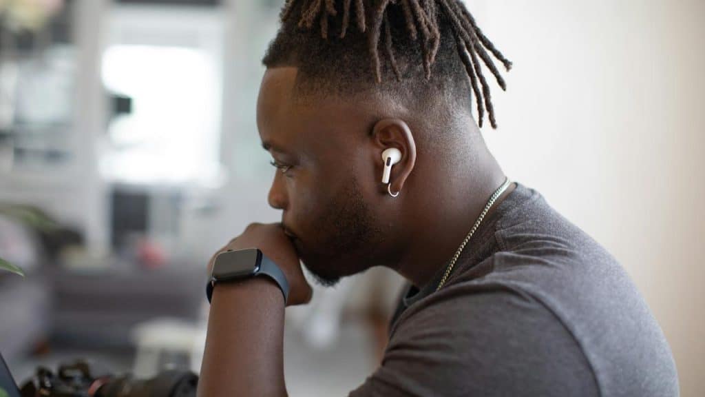 A man wearing earbuds and a smartwatch, looking pensive.