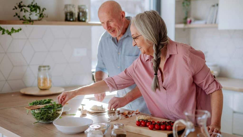 A senior couple cooking together in a bright kitchen.