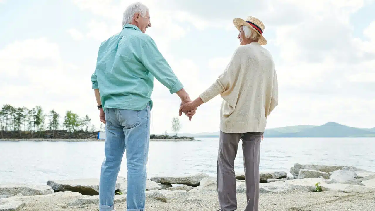 A senior couple holding hands and looking at each other by the water.