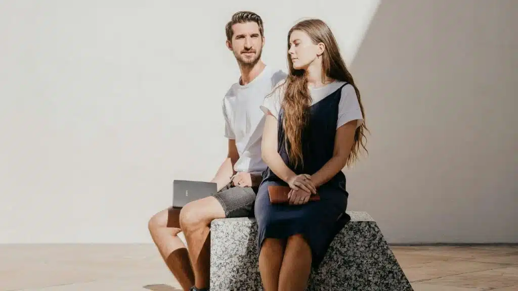 A couple sits on a stone bench, looking away from each other with distant expressions.
