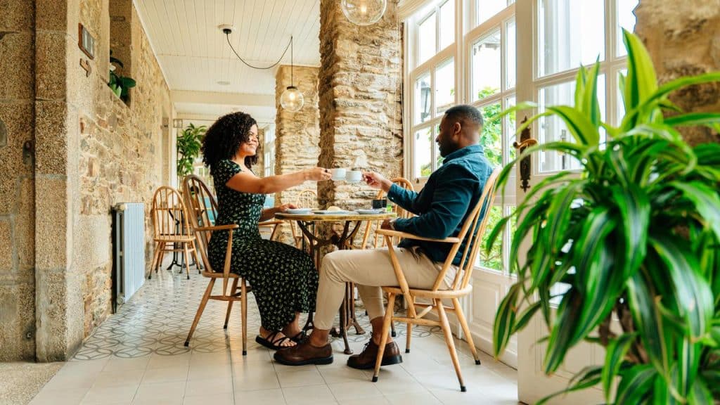 A couple clinking coffee cups at a cafe table.