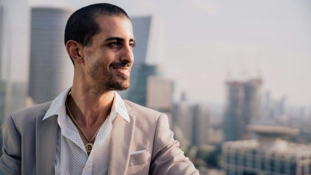 A man in a light blazer and necklace looking out over a city skyline.