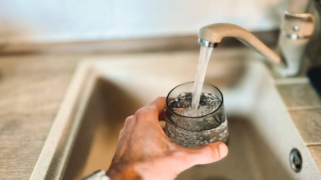 A hand filling a glass with tap water.