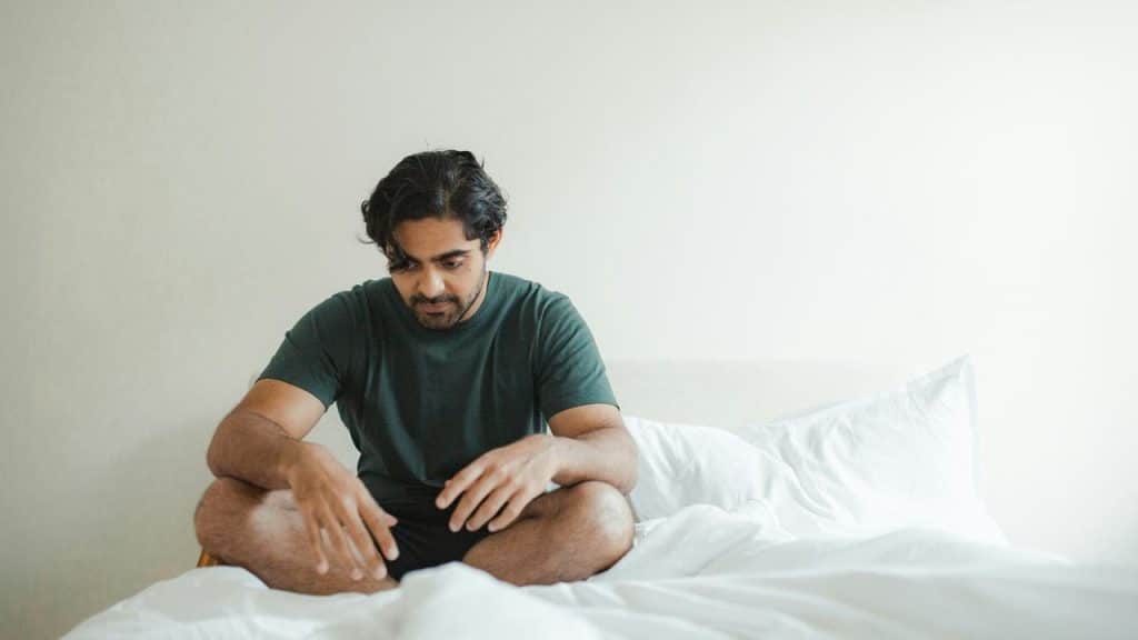A pensive man sitting cross-legged on a bed.