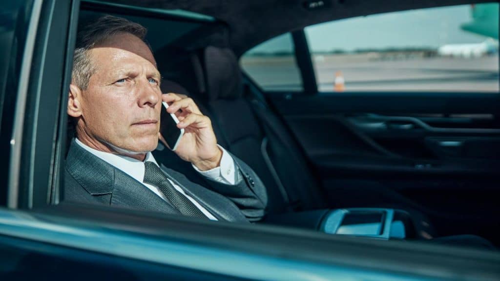 A businessman in a suit talking on a smartphone inside a car.