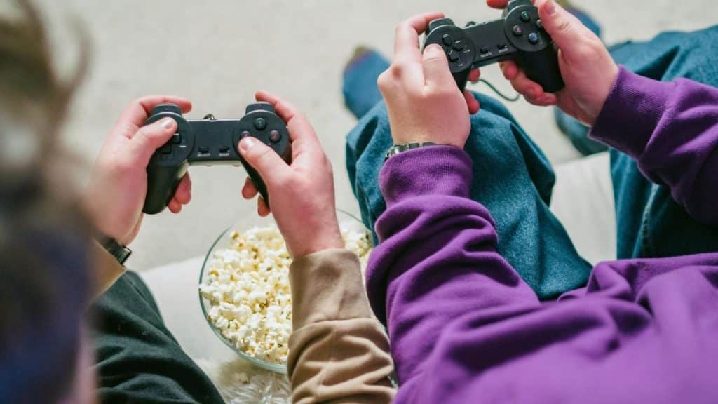 A pair of hands holding gaming controllers over a bowl of popcorn.