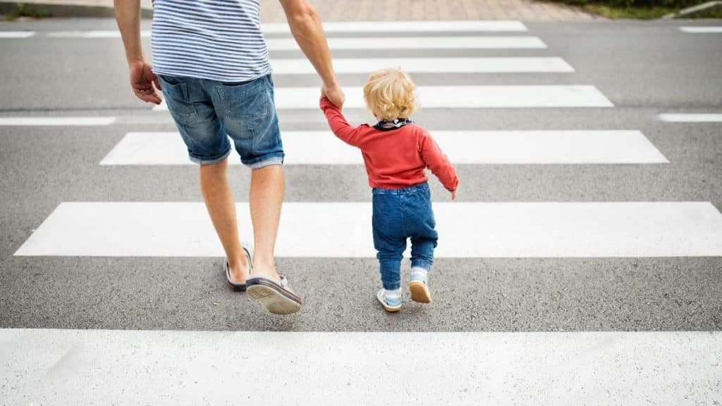 A man holding a toddler’s hand as they cross a crosswalk.