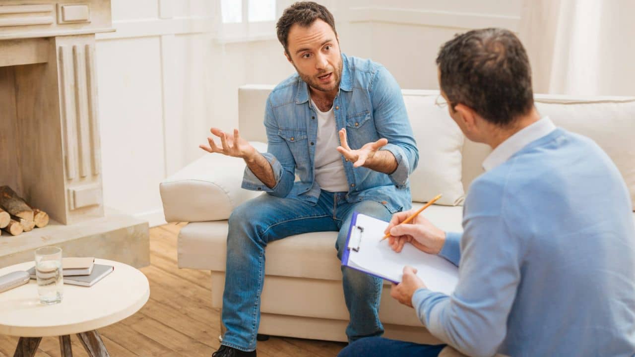 A man gestures while speaking to another man taking notes on a clipboard.