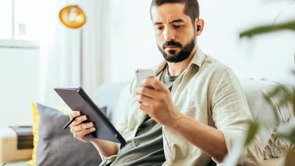 A man checking his phone while holding a tablet.