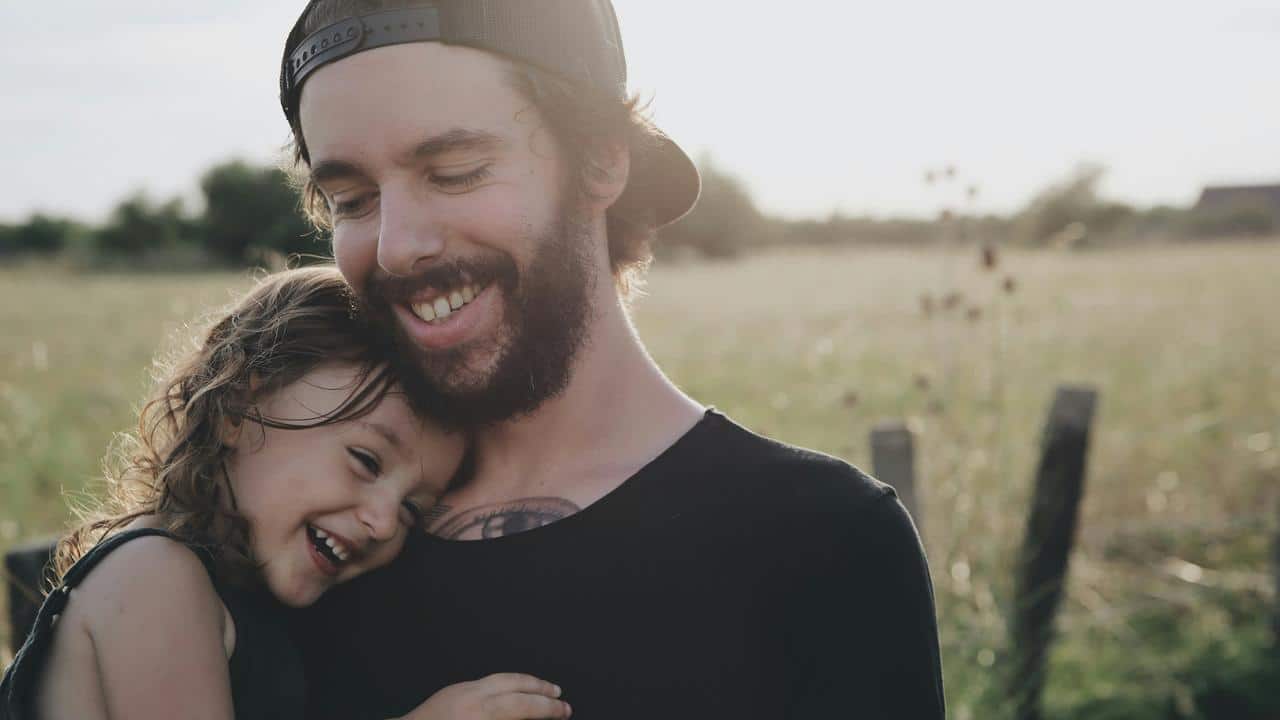 A bearded man holding a smiling child outdoors.