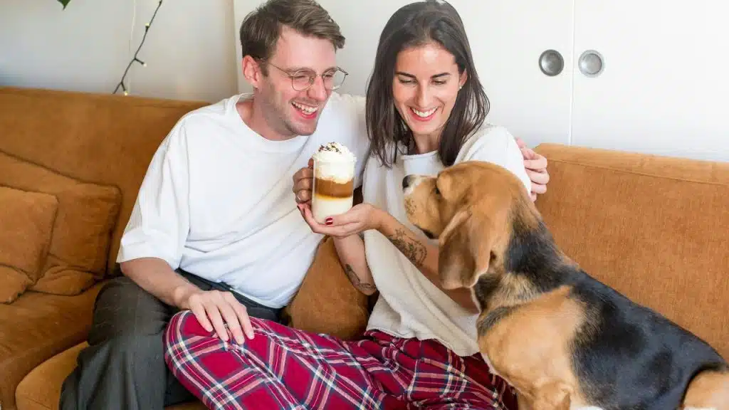 A couple offering a whipped cream–topped coffee to their dog.