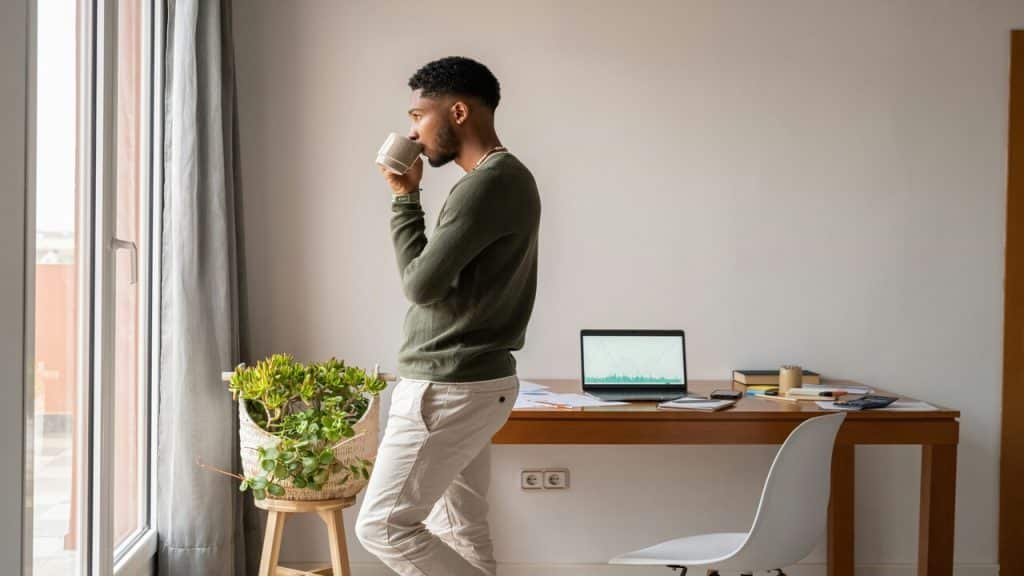 A man looking out the window while drinking coffee