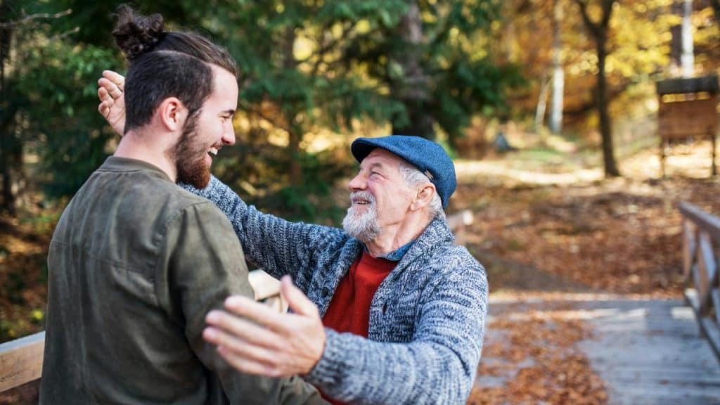 An elderly man embracing a younger man outdoors.