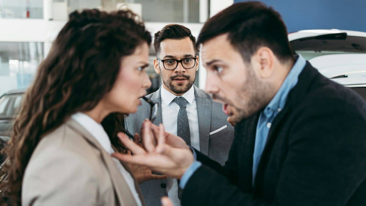 A man with an open mouth gestures while looking at a woman, and another man observes them.