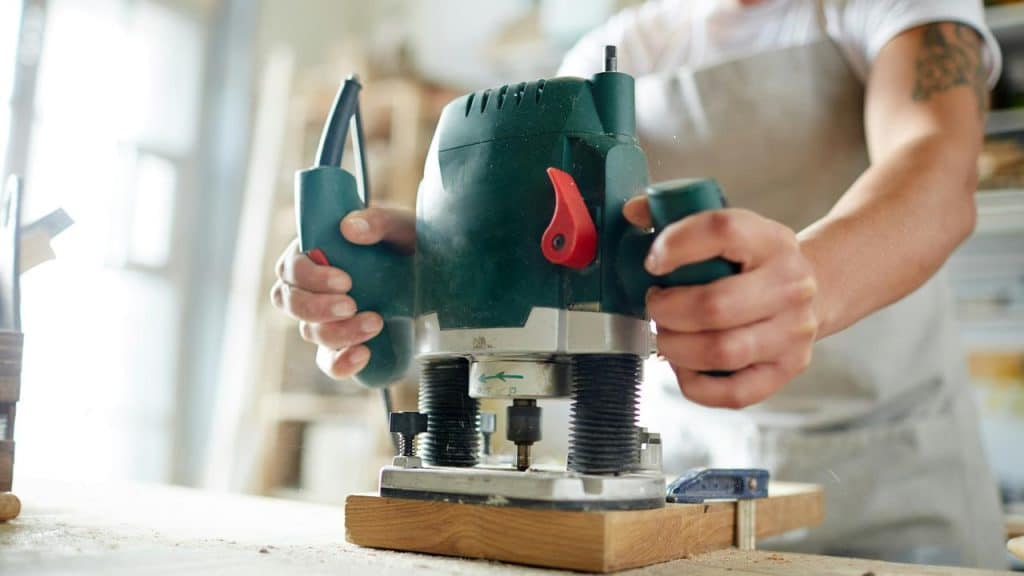 A woodworker holding a plunge router over a wooden board.