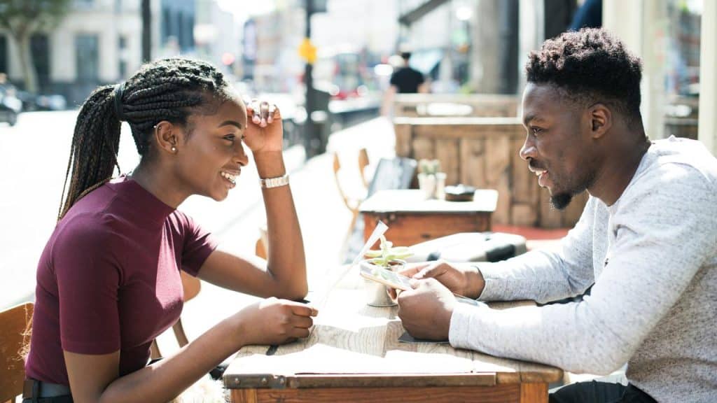 A man and woman chatting at a sunny sidewalk café table.