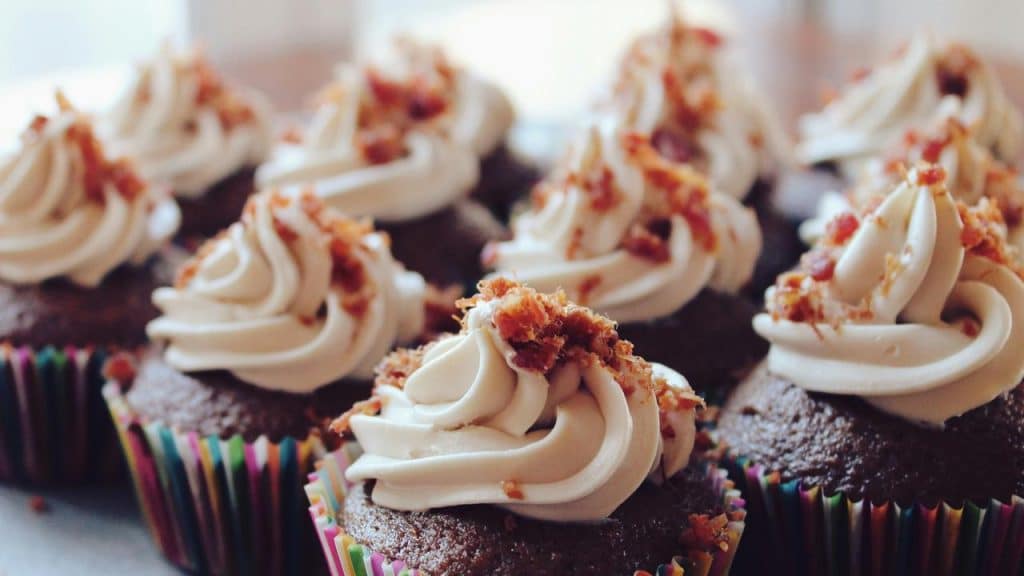 A row of chocolate cupcakes topped with swirled frosting and bacon bits.