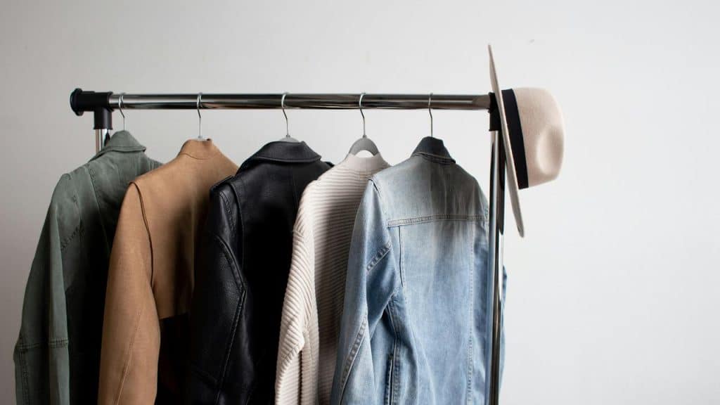 A rack with several jackets and a hat.