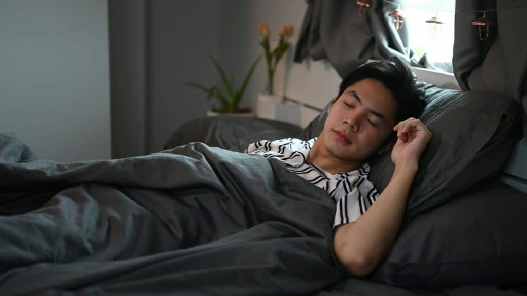 A man sleeps soundly in a bed, covered by a gray duvet.