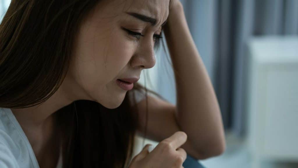 A distressed woman with long hair cries, a tear visible on her cheek.