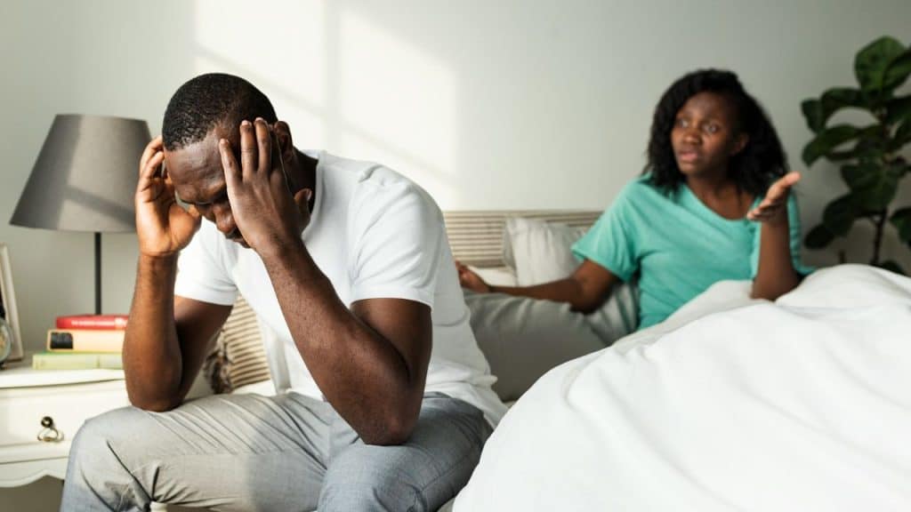 A man sits with his head in his hands, while a woman gestures angrily behind him.