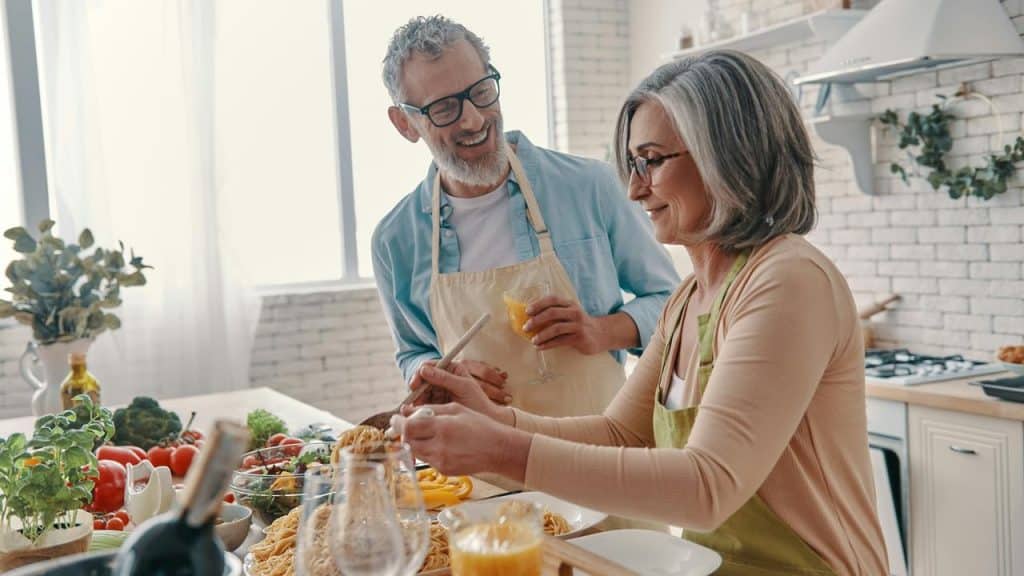 A senior couple cooking pasta together in a bright kitchen.