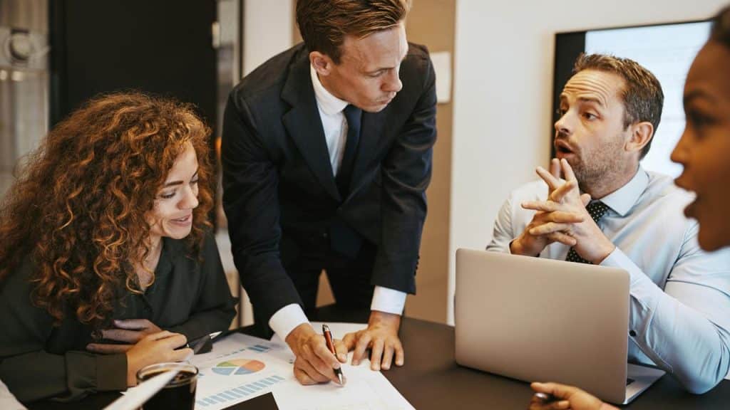 A business team gathered around a table reviewing charts and taking notes.