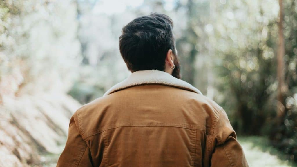 A man in a brown jacket with a white collar walks away from the camera.