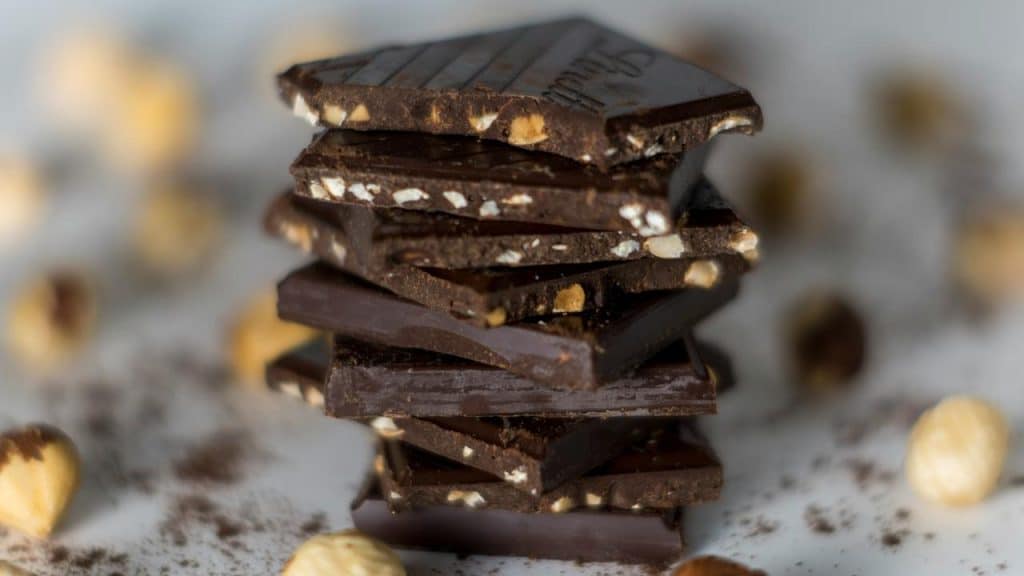 A stack of dark chocolate squares studded with hazelnuts.