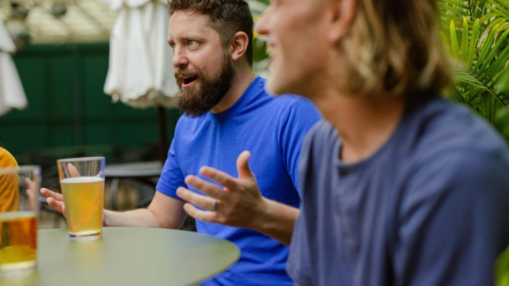 A man gesturing while talking over a beer with a friend.