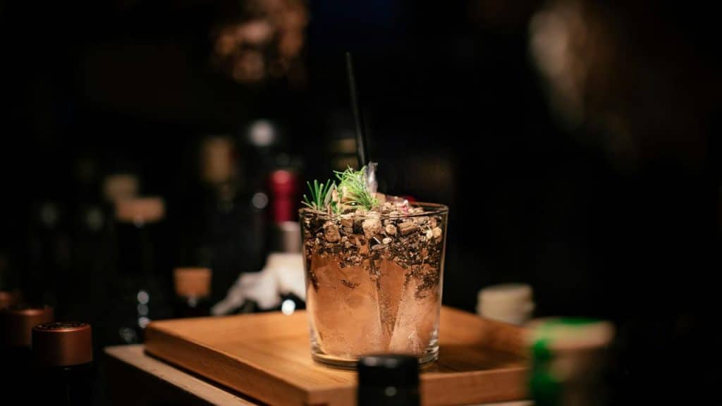A cocktail in a tumbler garnished with herbs and crumbled topping.