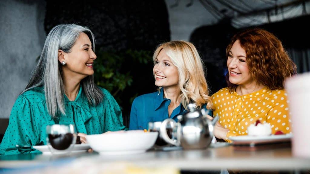 A trio of women smiling and chatting over tea.