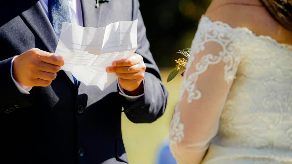 A groom reading vows from a crumpled paper to his bride.
